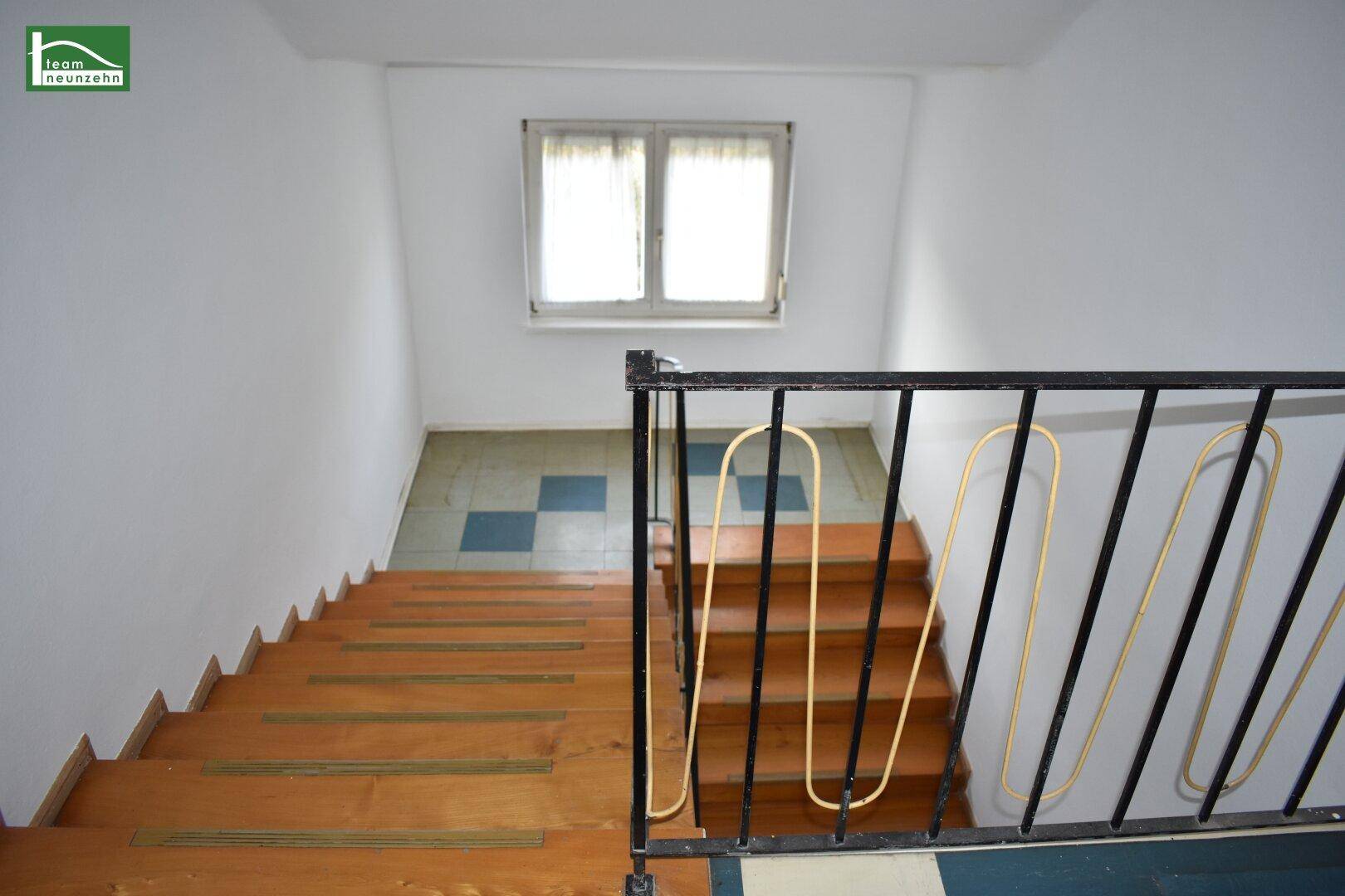 Treppenhaus mit Holzstufen, Metallgeländer und einem Fenster am oberen Ende.