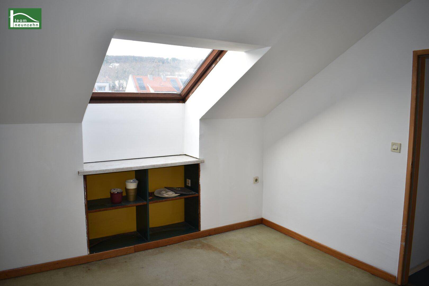 Dachzimmer mit Dachschräge, integriertem Regal und einem Dachfenster für Tageslicht.