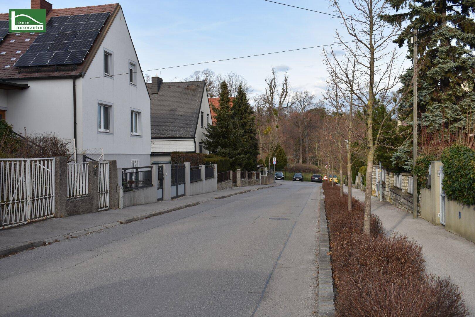 Ruhige Wohnstraße mit Häusern, Bäumen und gepflegten Vorgärten.