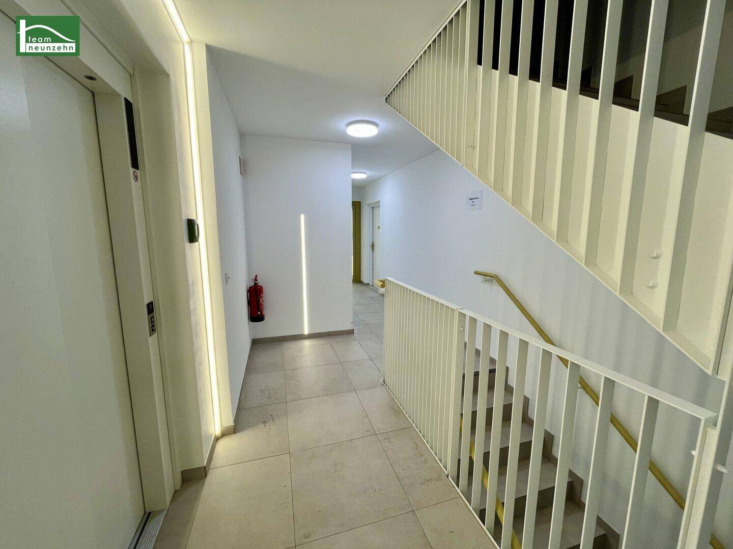 Treppenhaus und Flur mit Aufzug, heller Beleuchtung und modernen Geländern.