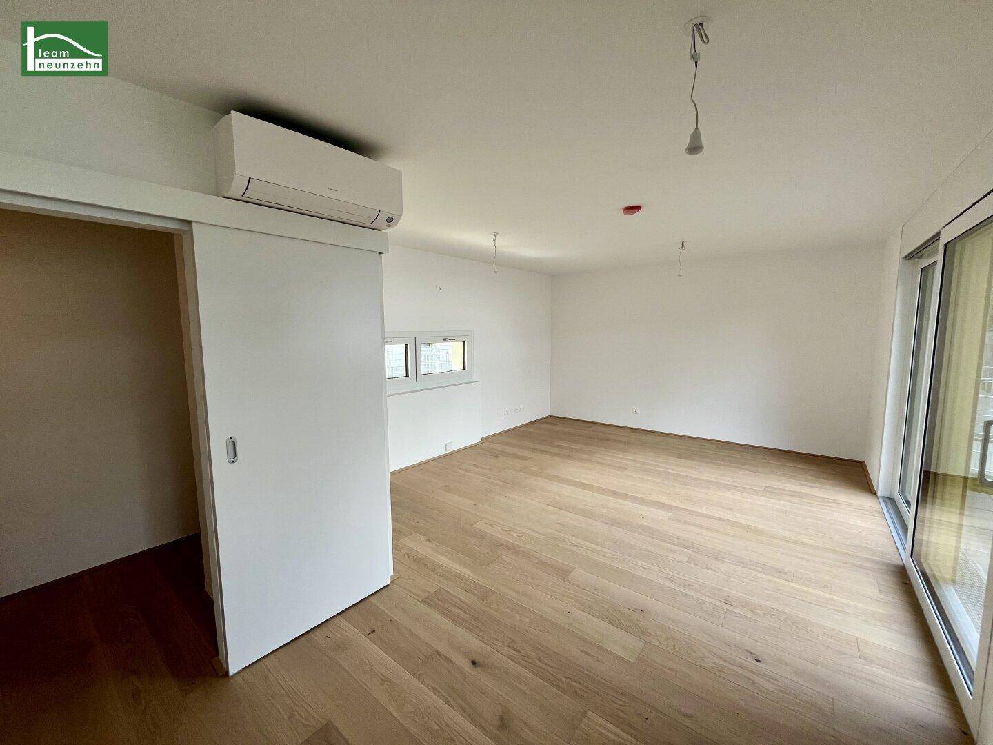 Geräumiger, heller Raum mit Holzboden und Klimaanlage, ideal als Wohnbereich.