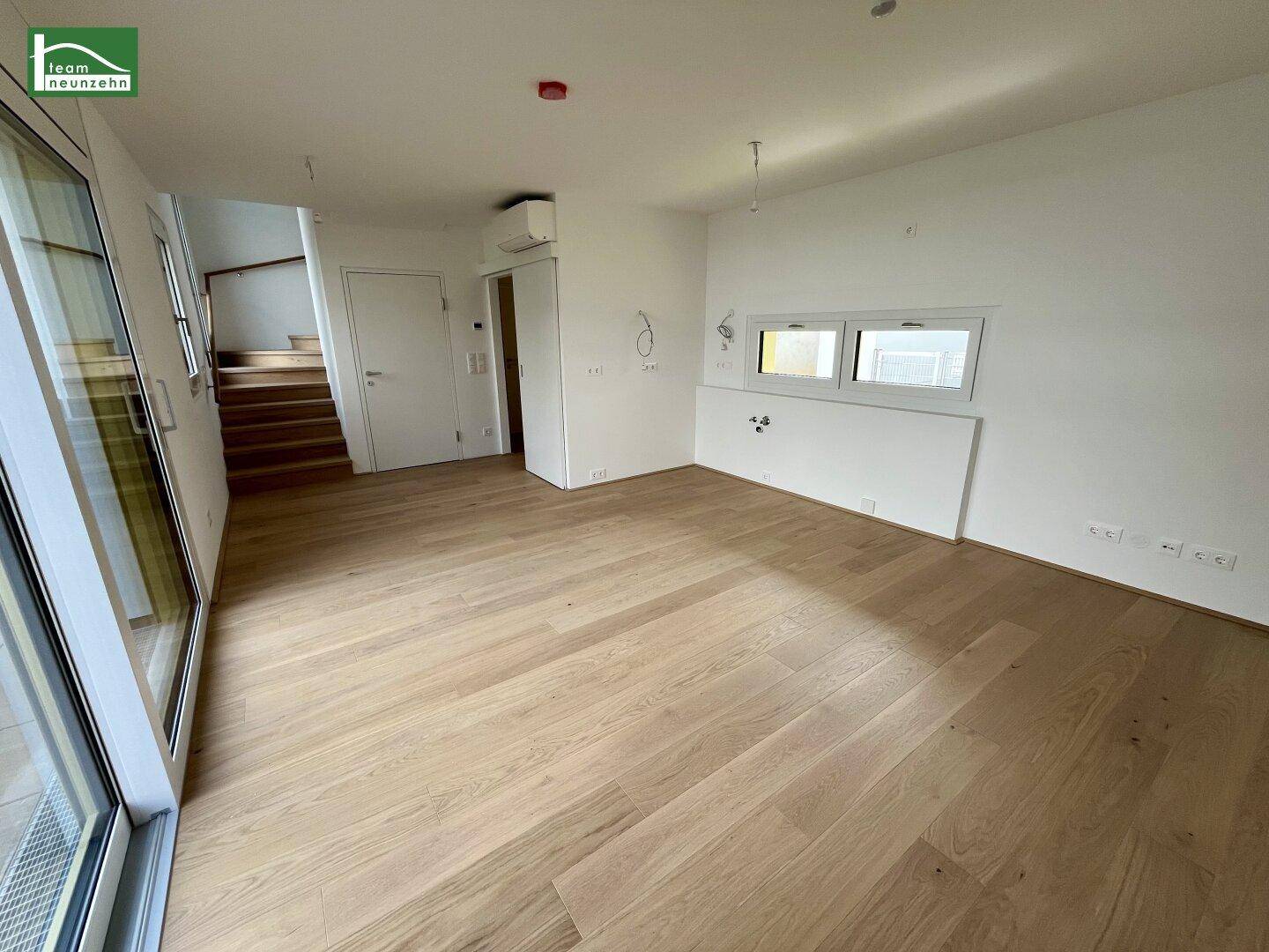 Heller Wohnbereich mit Holzboden, großen Fenstern und Treppenzugang.