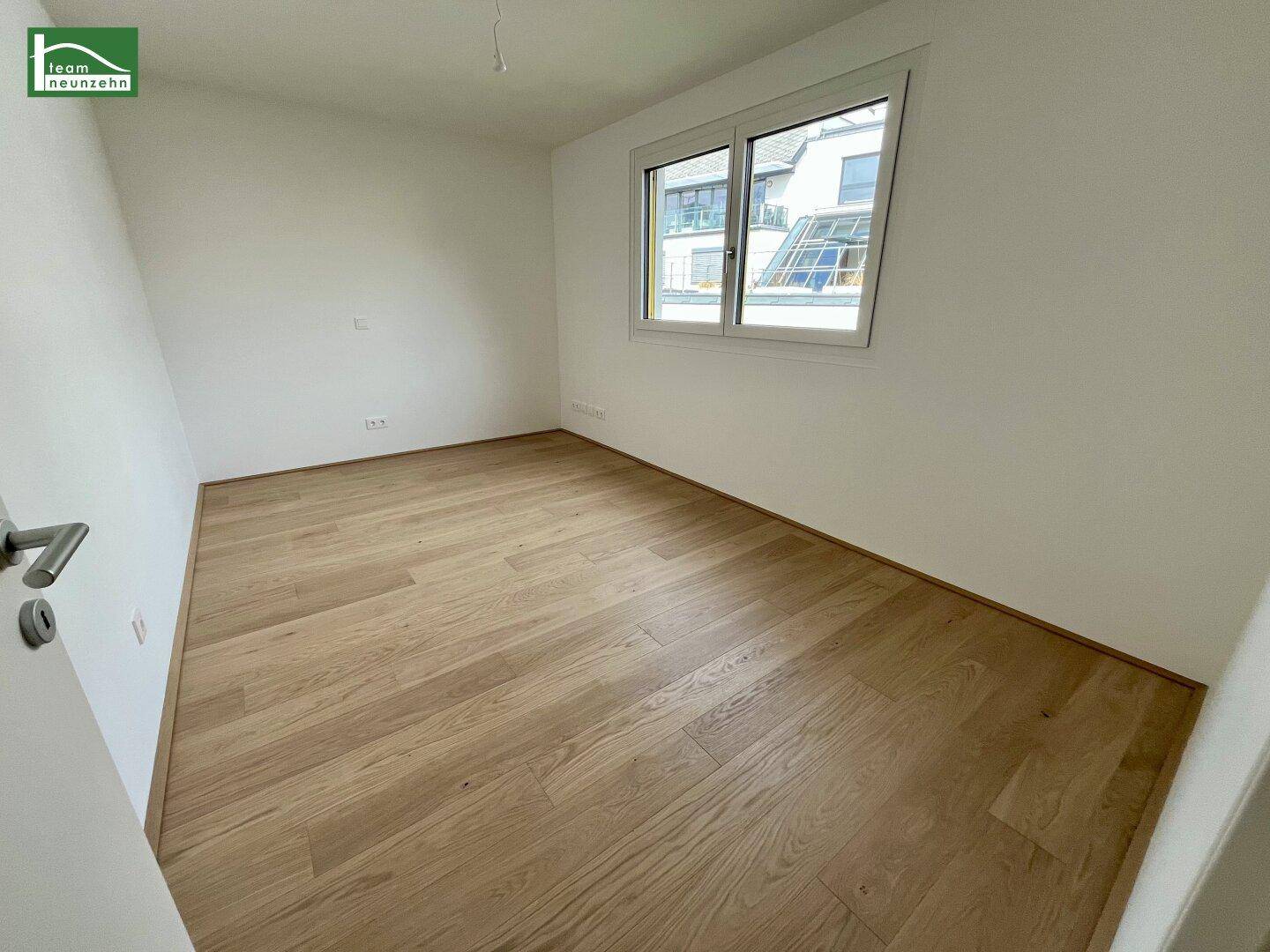 Freundliches Zimmer mit Holzboden und Blick ins Grüne.