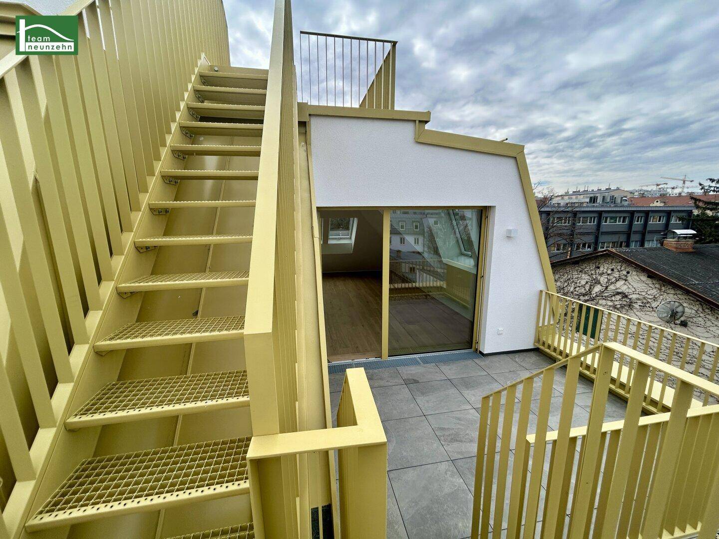 Geräumige Dachterrasse mit gelben Geländern und Treppe zu einer weiteren Ebene, bietet Stadtblick.