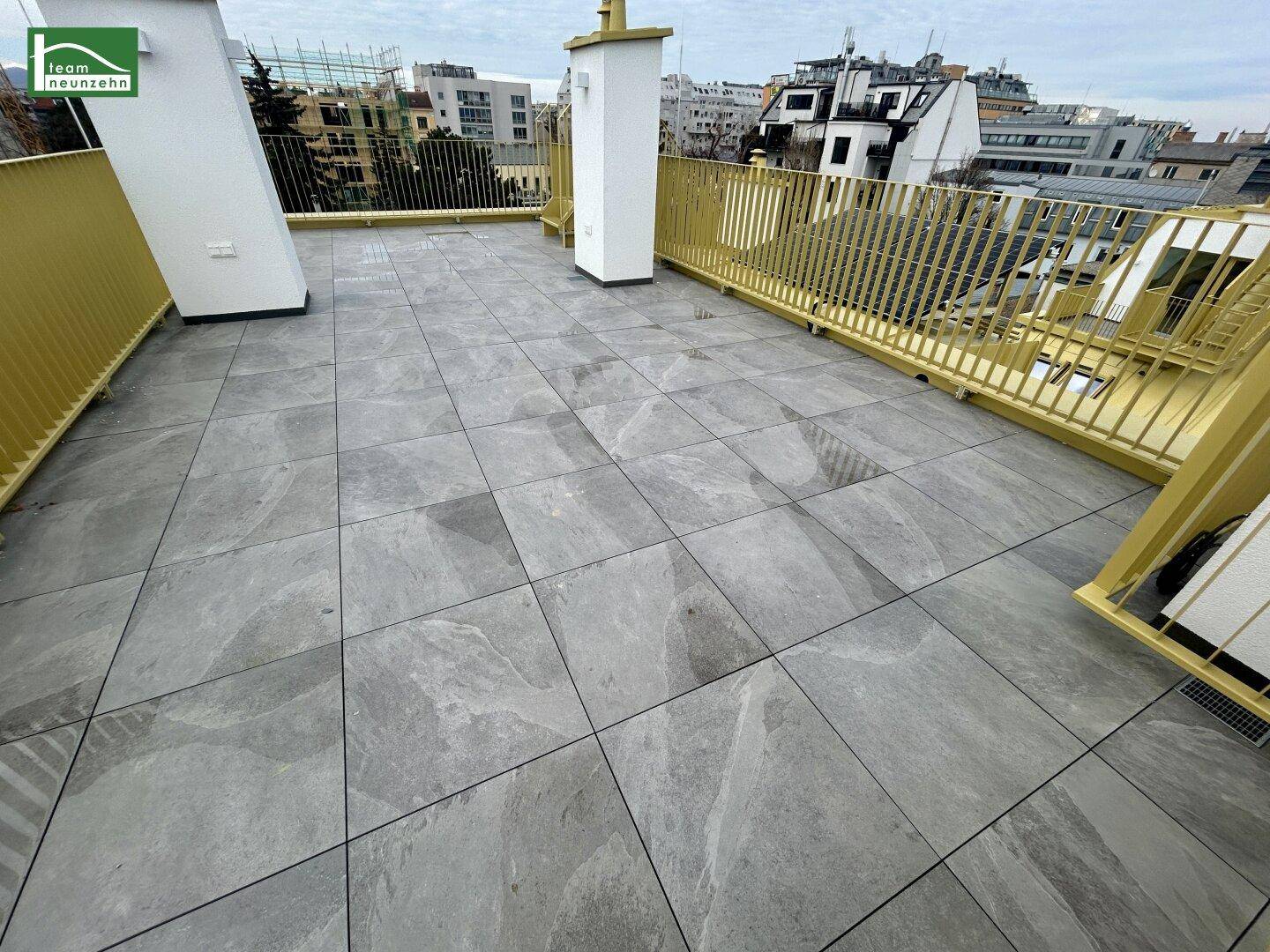 Weitläufige Dachterrasse mit modernen Fliesen und gelben Geländern, ideal für Entspannung im Freien.