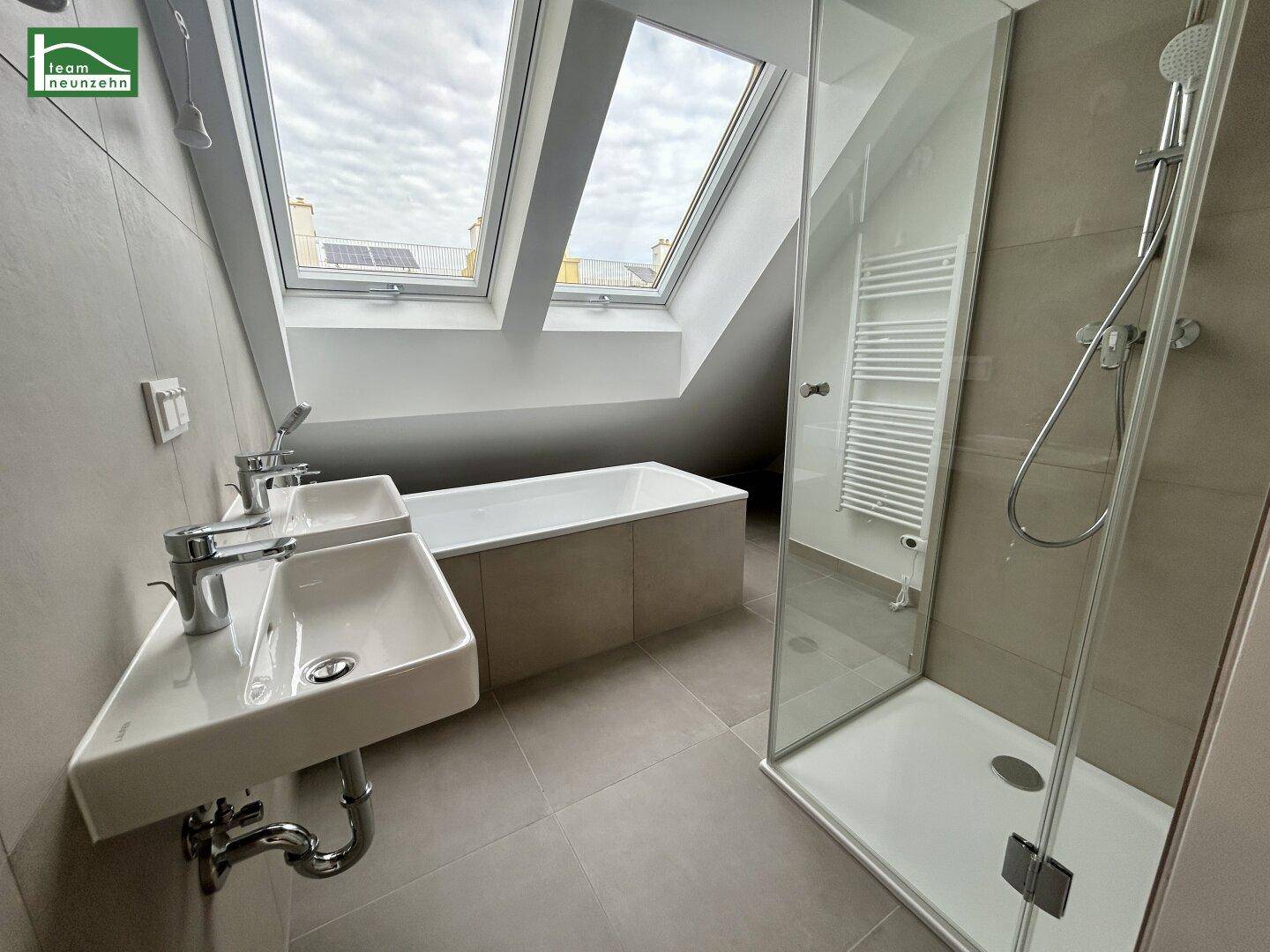 Modernes Badezimmer im Dachgeschoss mit Doppelwaschbecken, Badewanne, Dusche und Dachfenstern.