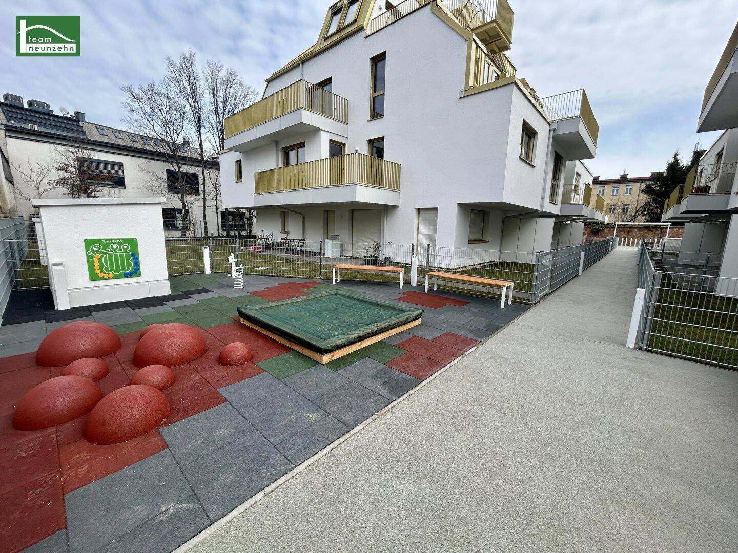 Gemeinschaftlicher Spielplatz mit Sandkasten und Sitzbänken im Außenbereich der Wohnanlage.