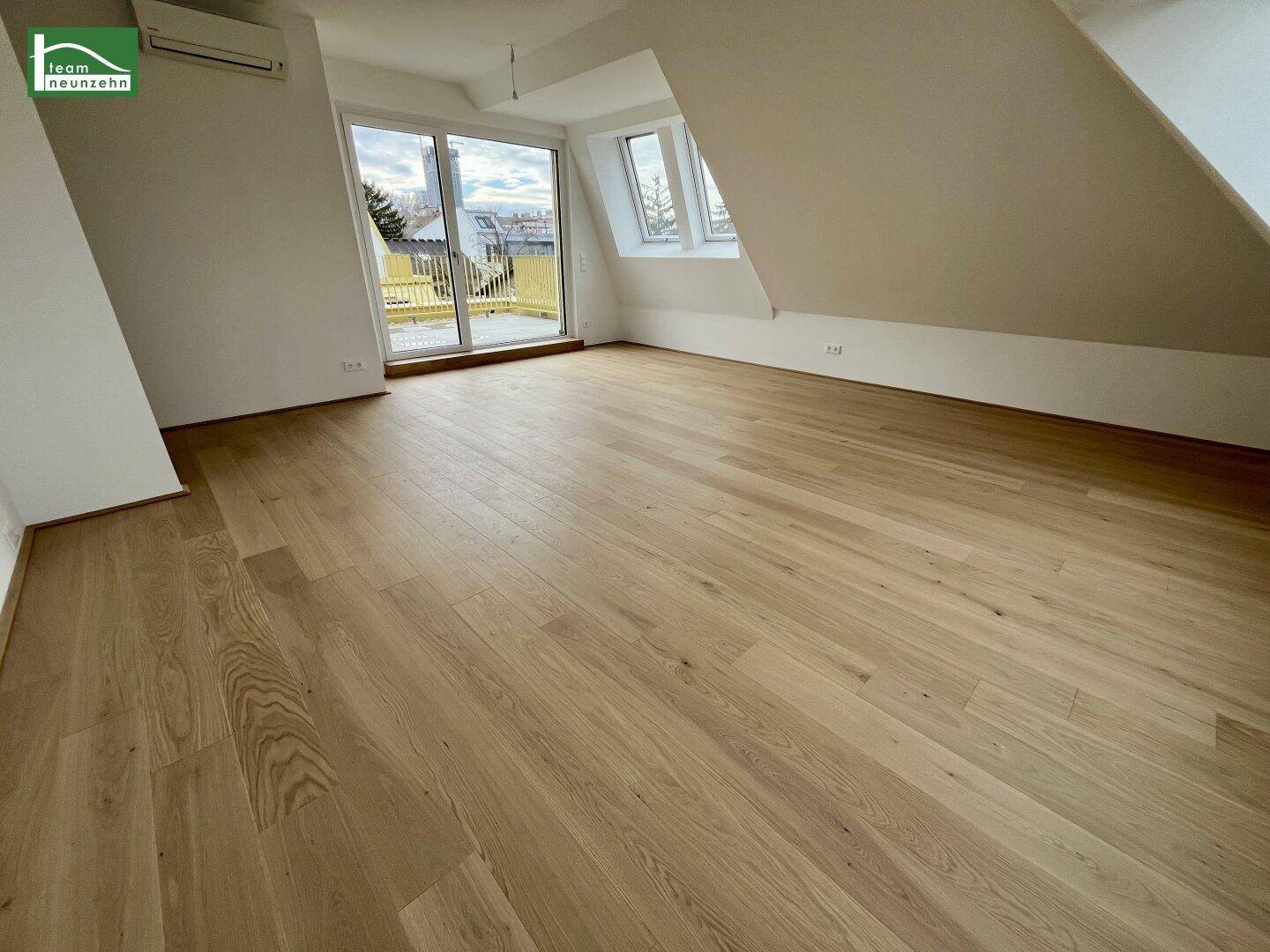 Helles Zimmer im Dachgeschoss mit Holzboden, Schrägdecken und Zugang zu einer Terrasse.