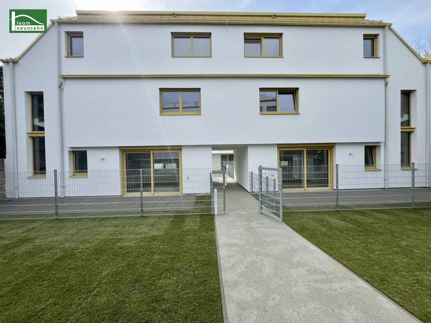 Moderne Wohnanlage mit weißer Fassade, gelben Akzenten und Grünflächen.