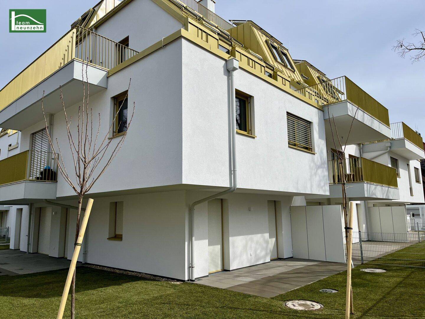 Moderne Wohnanlage mit weißer Fassade, gelben Balkonen und gepflegten Grünflächen.