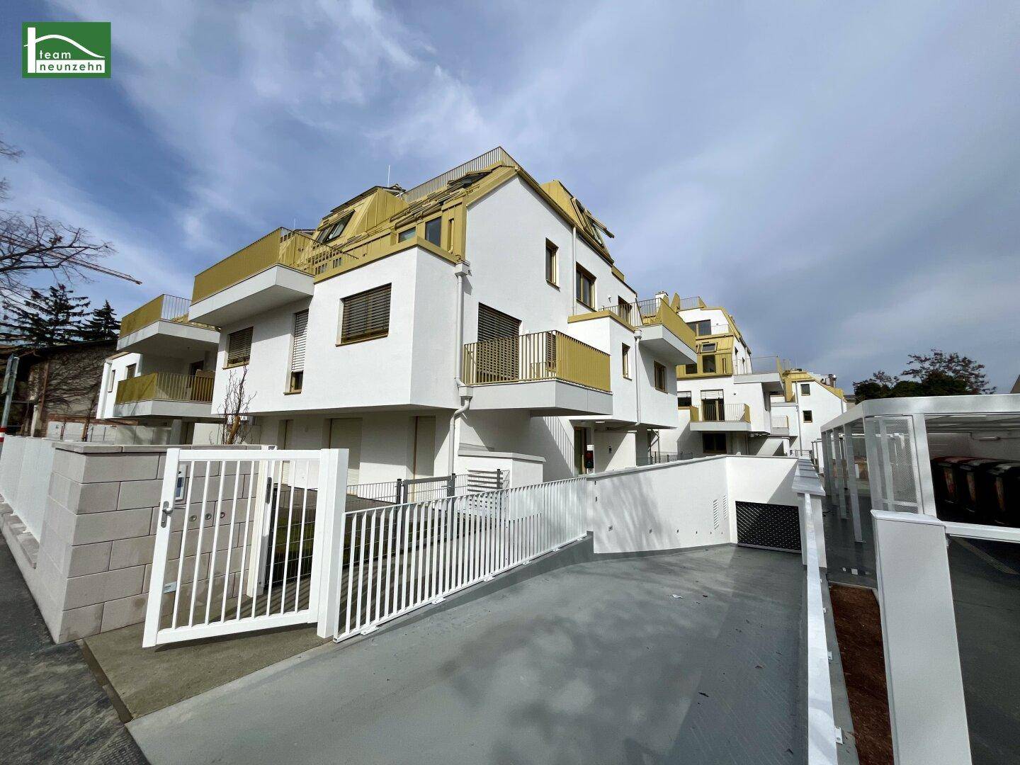 Moderne Wohnanlage mit weißer Fassade, gelben Akzenten und Zufahrt zur Tiefgarage.