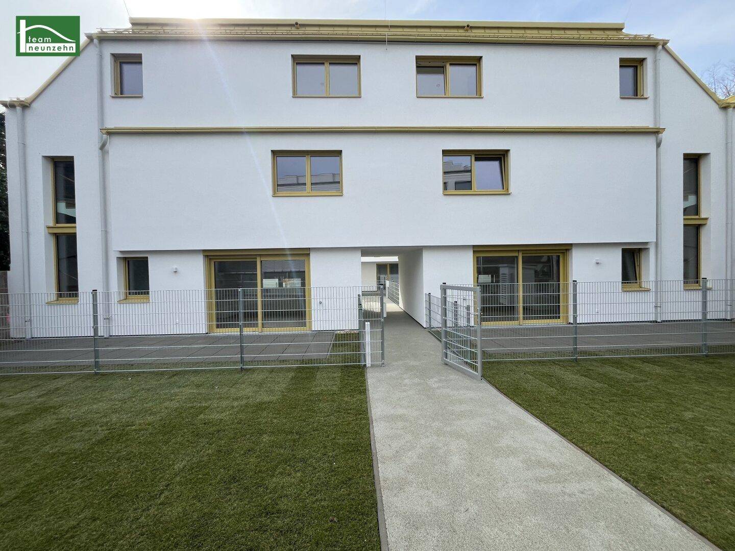 Moderne Gebäudefassade mit großen Fenstern und gepflegter Rasenfläche im Vordergrund.