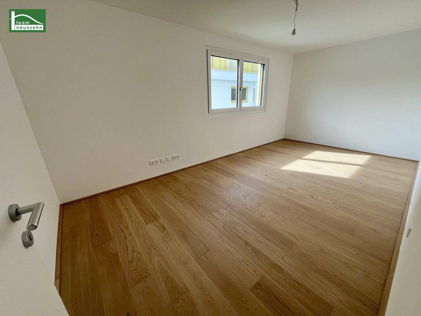 Helles Schlafzimmer mit Holzboden und großem Fenster, ideal für natürliche Belichtung.