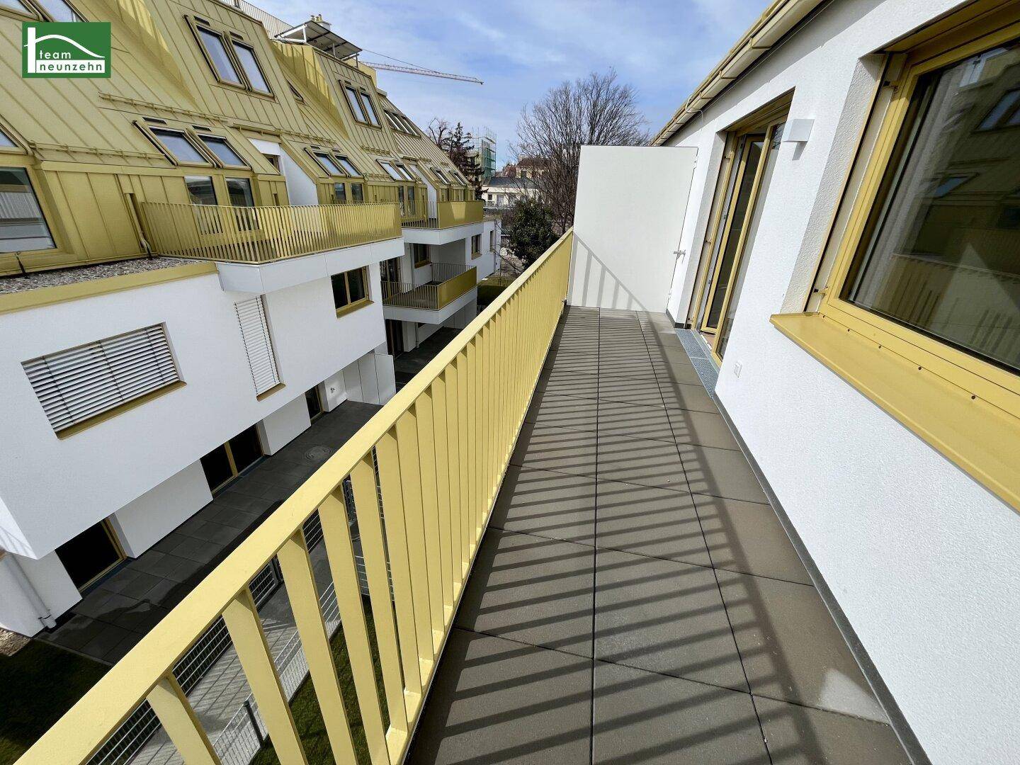 Langer Balkon mit gelbem Geländer und Blick auf die umliegenden Gebäude.