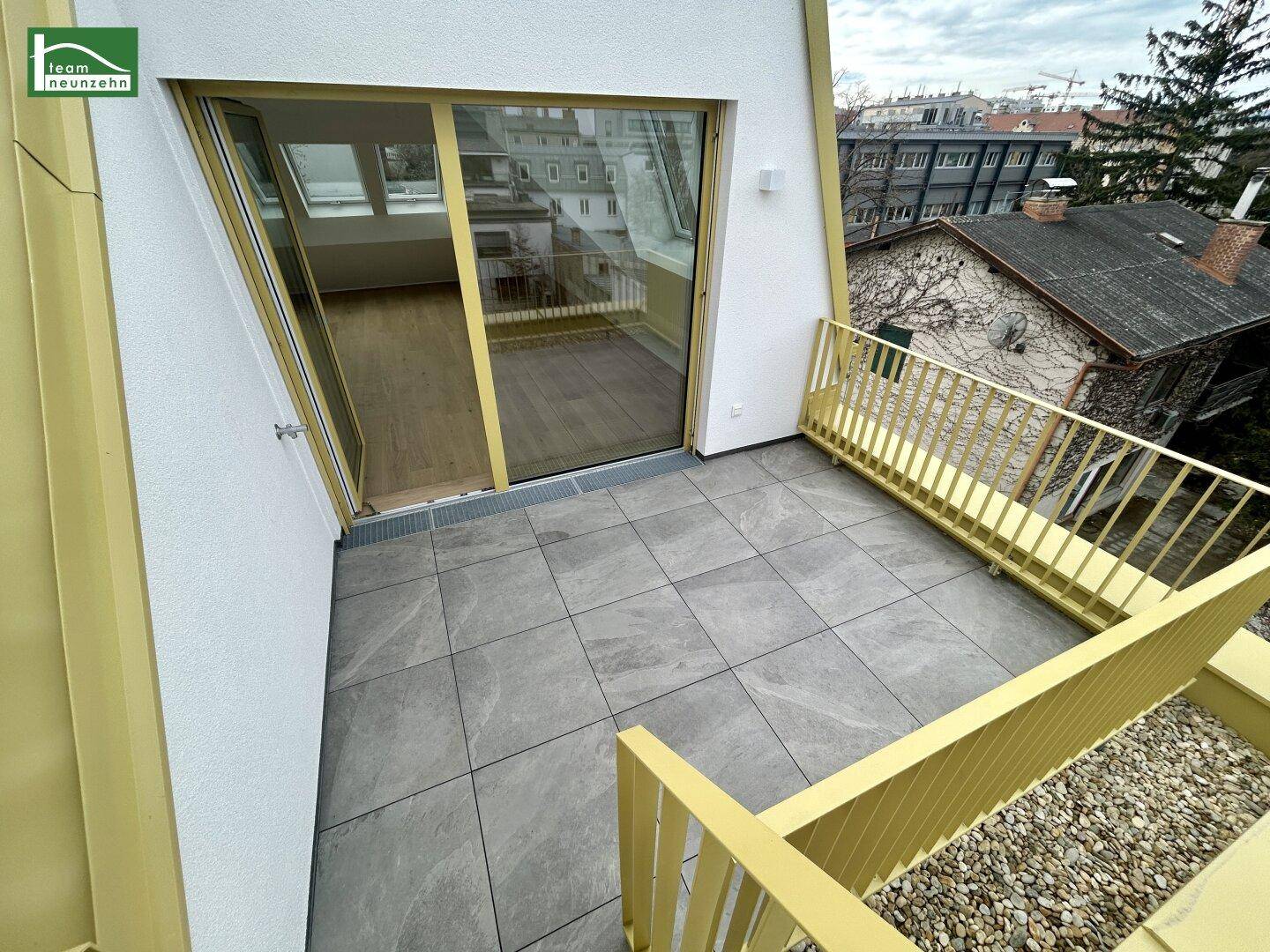 Obere Terrasse mit Blick auf eine darunterliegende Terrasse und die moderne Gebäudefassade.