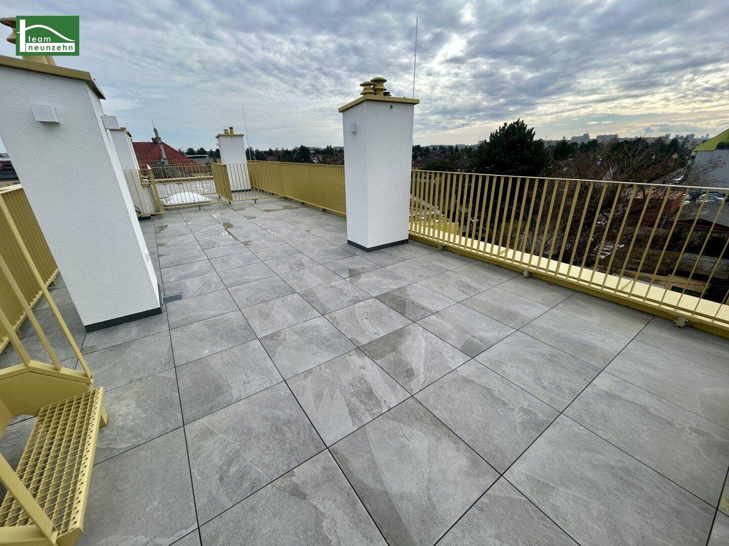 Weitläufige Dachterrasse mit modernen Fliesen und gelbem Geländer, bietet viel Platz im Freien.