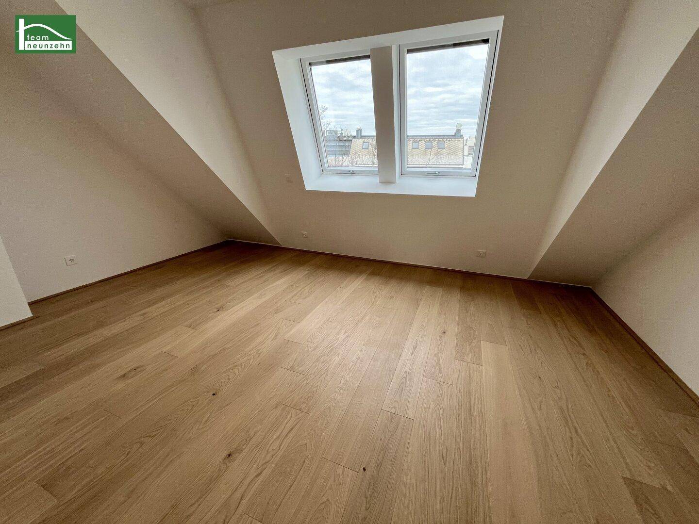 Gemütliches Zimmer im Dachgeschoss mit Holzboden, Schrägdecken und einem großen Dachfenster.