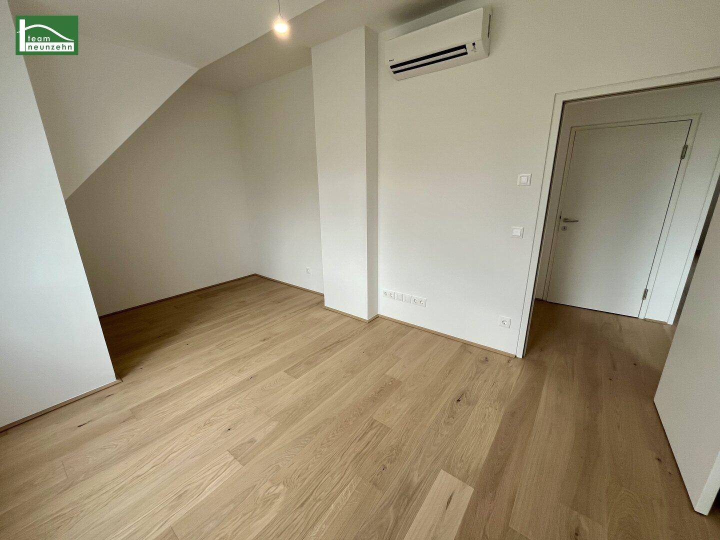 Zimmer im Dachgeschoss mit Holzboden, weißen Wänden und Klimaanlage.