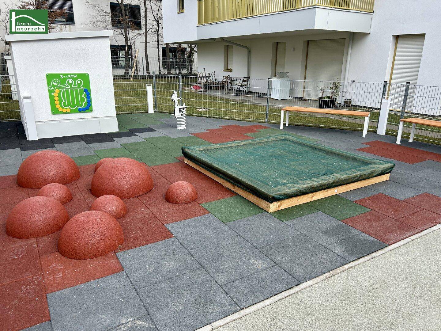 Kinderspielplatz mit Sandkasten, Gummiboden und Sitzbänken für die Bewohner.