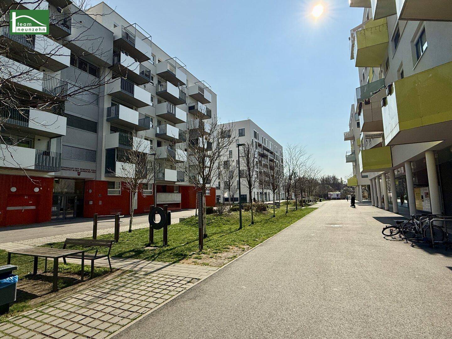 Weitläufige Promenade zwischen modernen Wohngebäuden mit Bäumen und Sitzgelegenheiten.