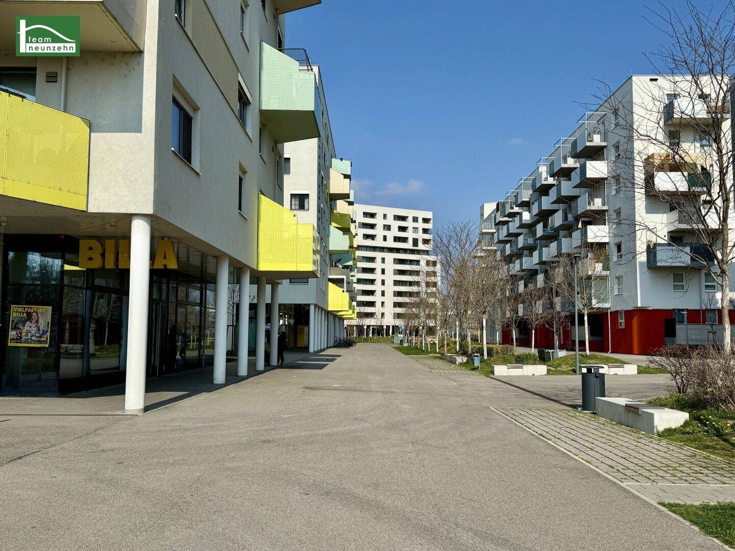 Fußgängerzone zwischen modernen Wohn- und Geschäftsgebäuden mit einem Supermarkt im Erdgeschoss.