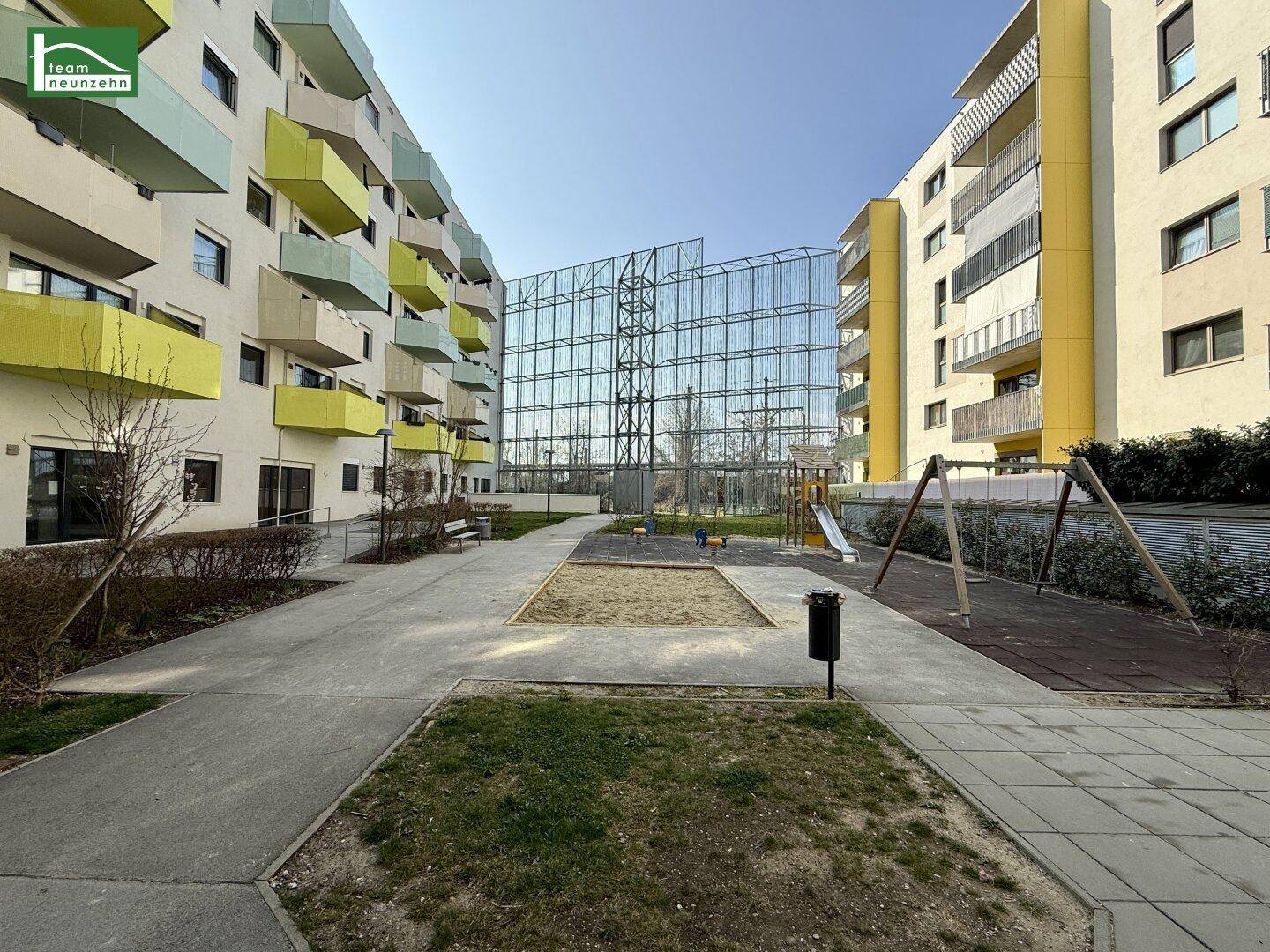 Moderner Innenhof mit Kinderspielplatz, umgeben von Wohngebäuden mit farbigen Balkonen.