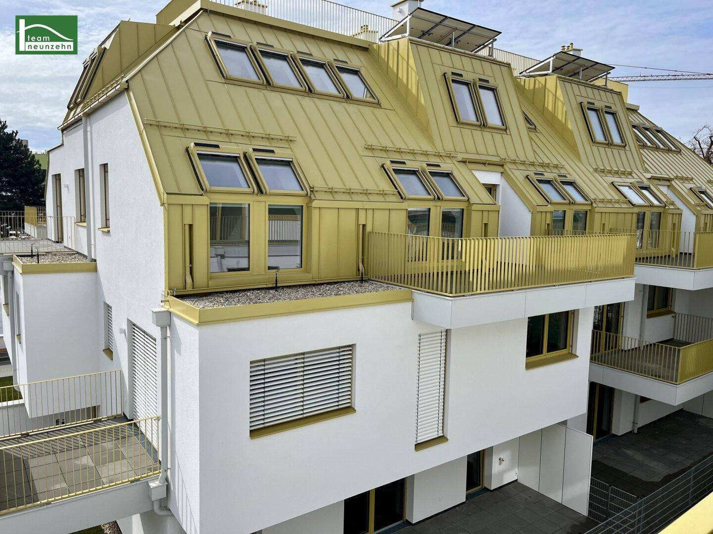 Moderne Wohnanlage mit weißer Fassade, goldenem Dach und mehreren Balkonen unter hellem Himmel.