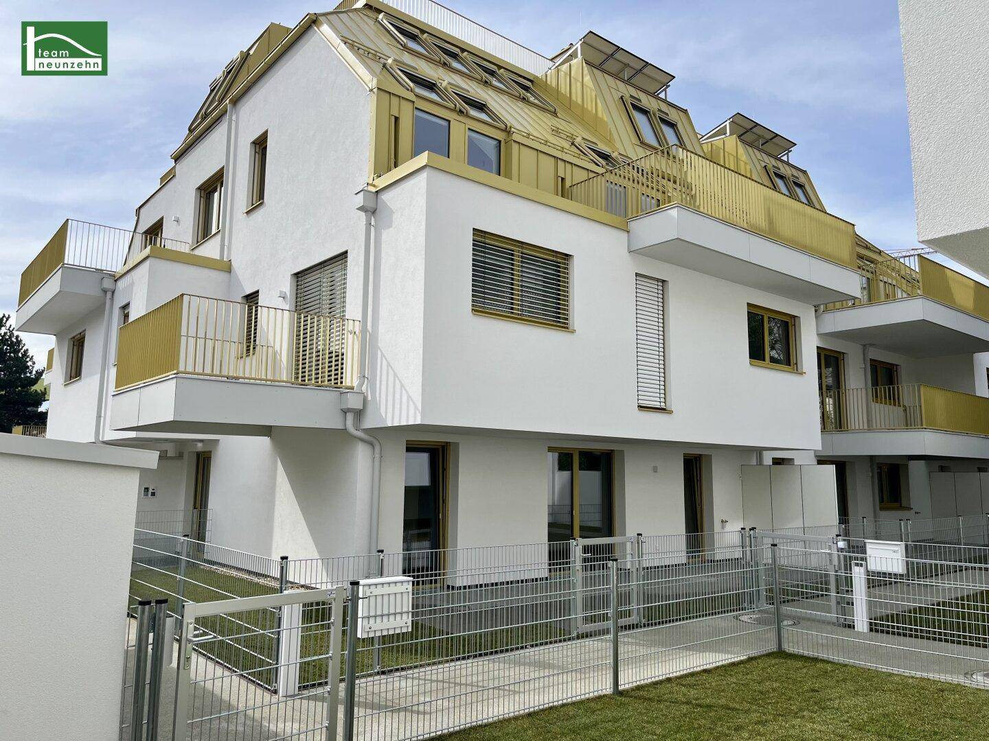 Modernes Wohngebäude mit goldfarbenem Dach, weißen Fassaden und gepflegter Grünfläche im Vordergrund.