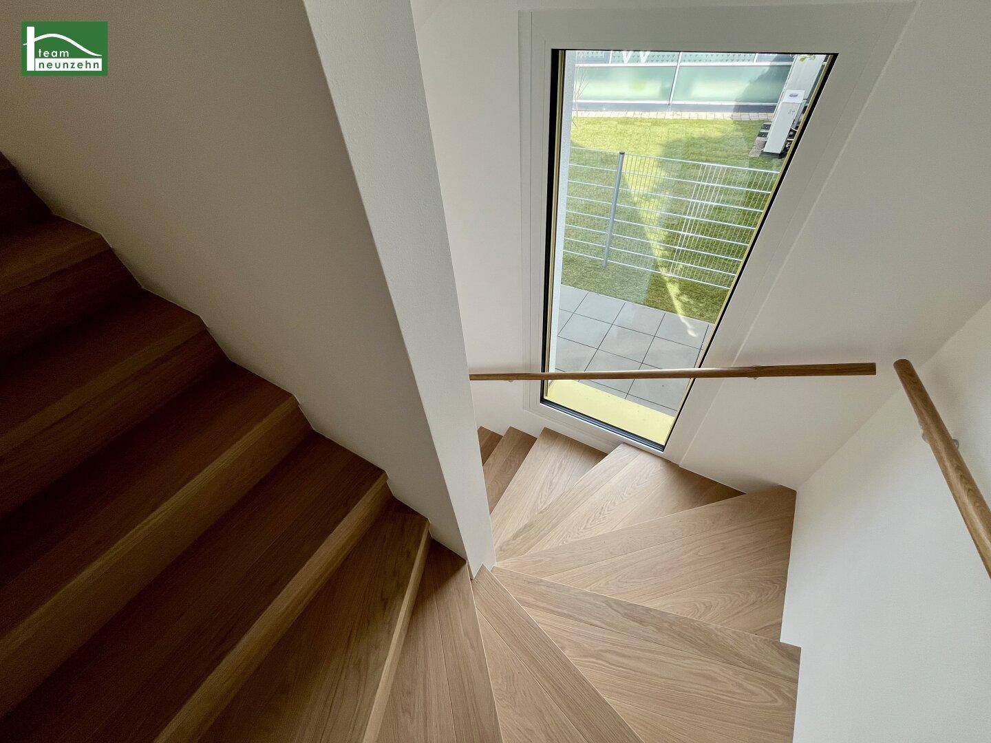 Elegante Wendeltreppe aus Holz mit großem Fenster, das viel Tageslicht hereinlässt.