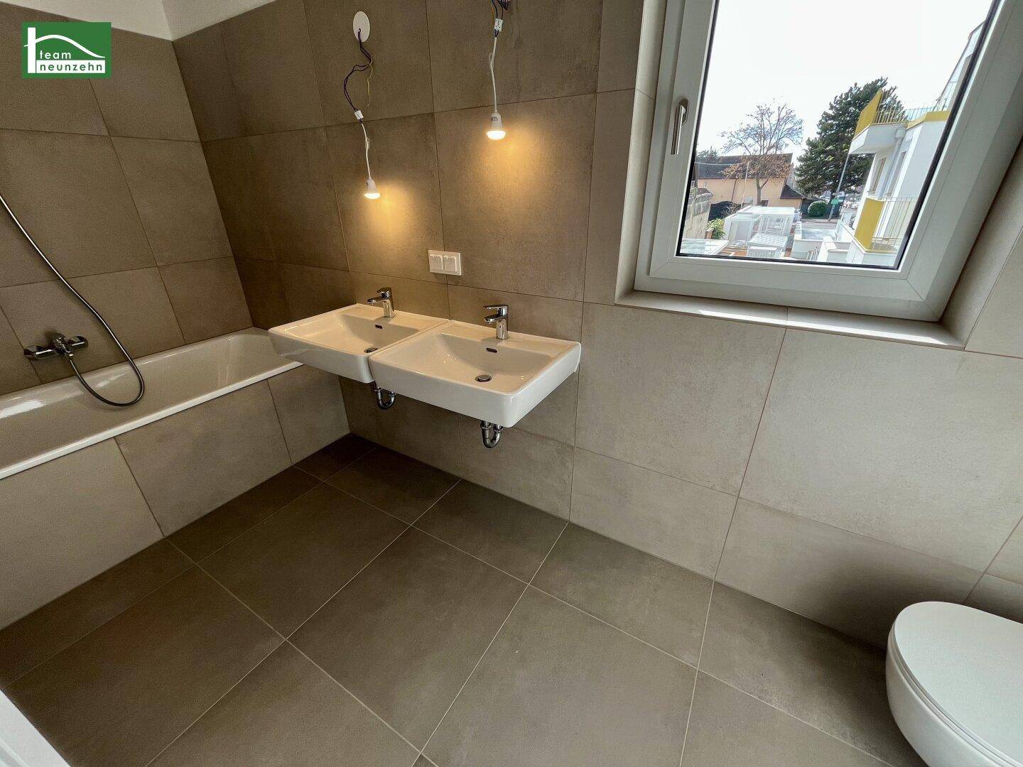 Modernes Badezimmer mit zwei Waschbecken, Badewanne und Fenster für Tageslicht.
