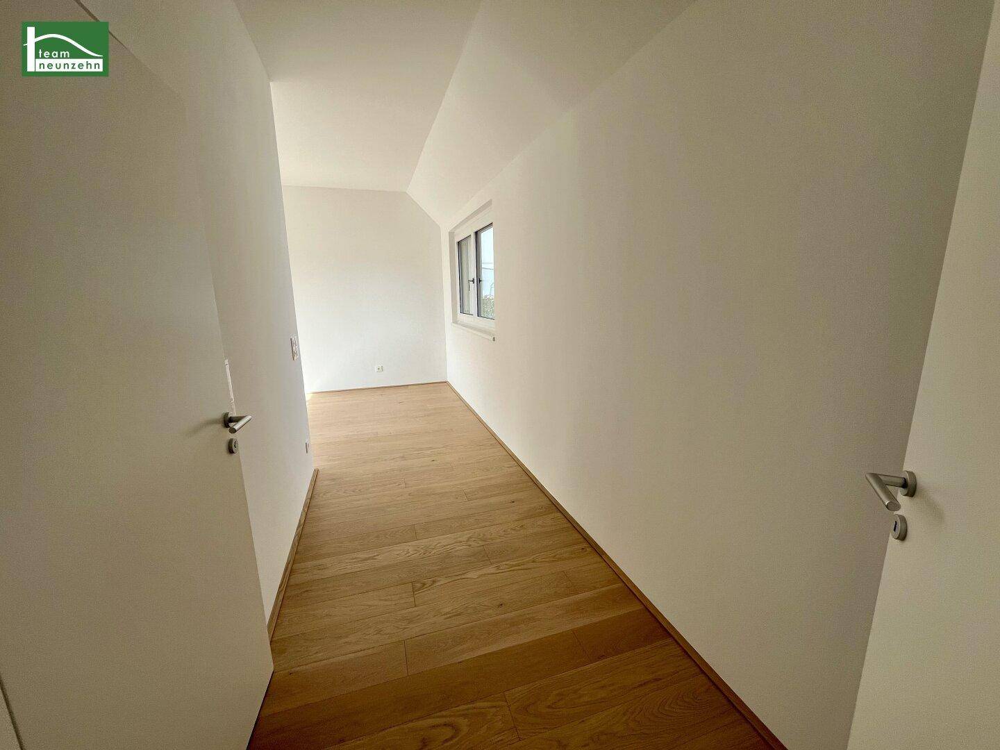 Heller Flur im Dachgeschoss mit Holzboden und Fenster, das Tageslicht spendet.