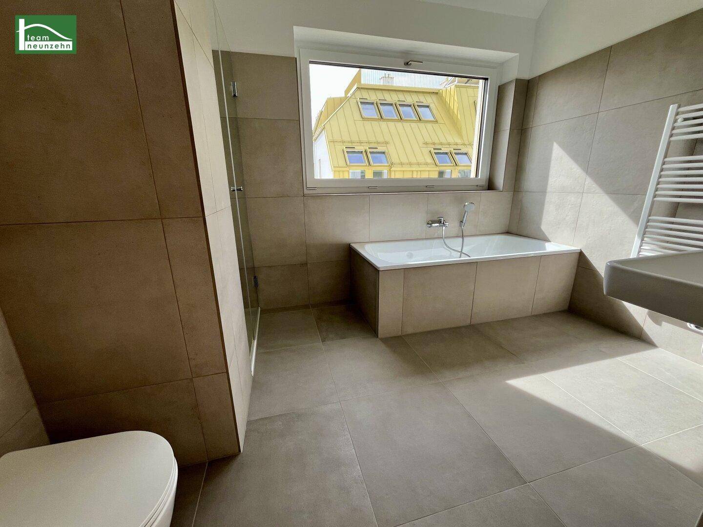 Helles Badezimmer mit Badewanne, Duschkabine und Fenster, modern gefliest.