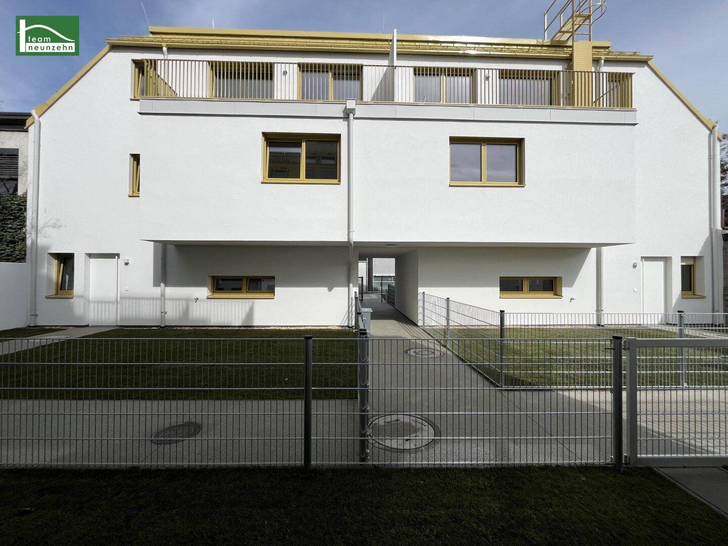Moderne Gebäudefassade mit weißem Putz, gelben Fensterrahmen und gepflegtem Vorgarten.