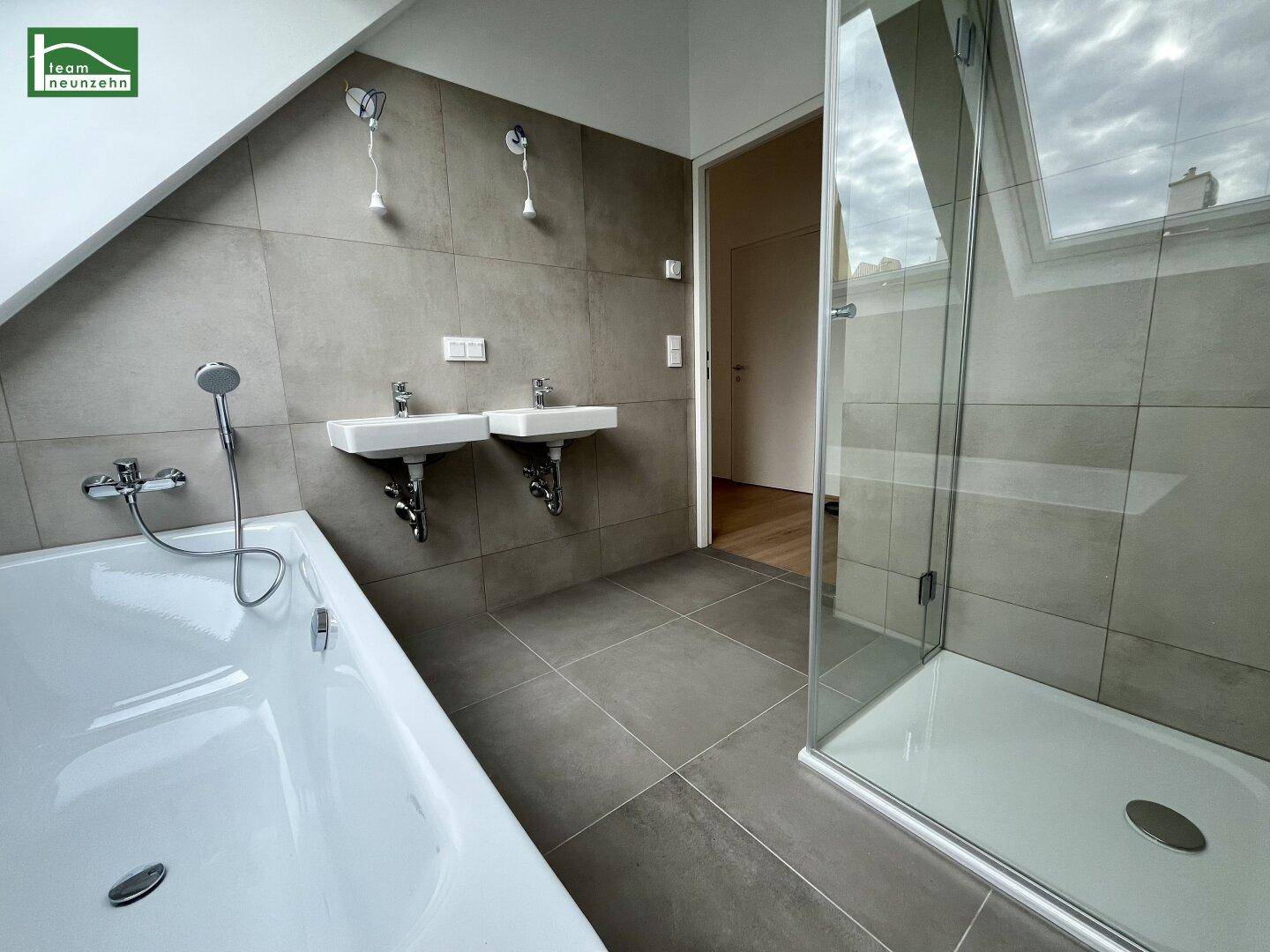 Helles Badezimmer mit Badewanne, Dusche und Doppelwaschbecken, modern gefliest und gut beleuchtet.