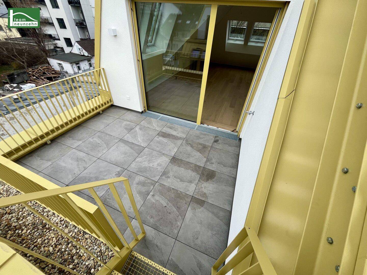 Geräumige geflieste Terrasse mit gelbem Geländer und Treppenzugang, ideal für Entspannung.