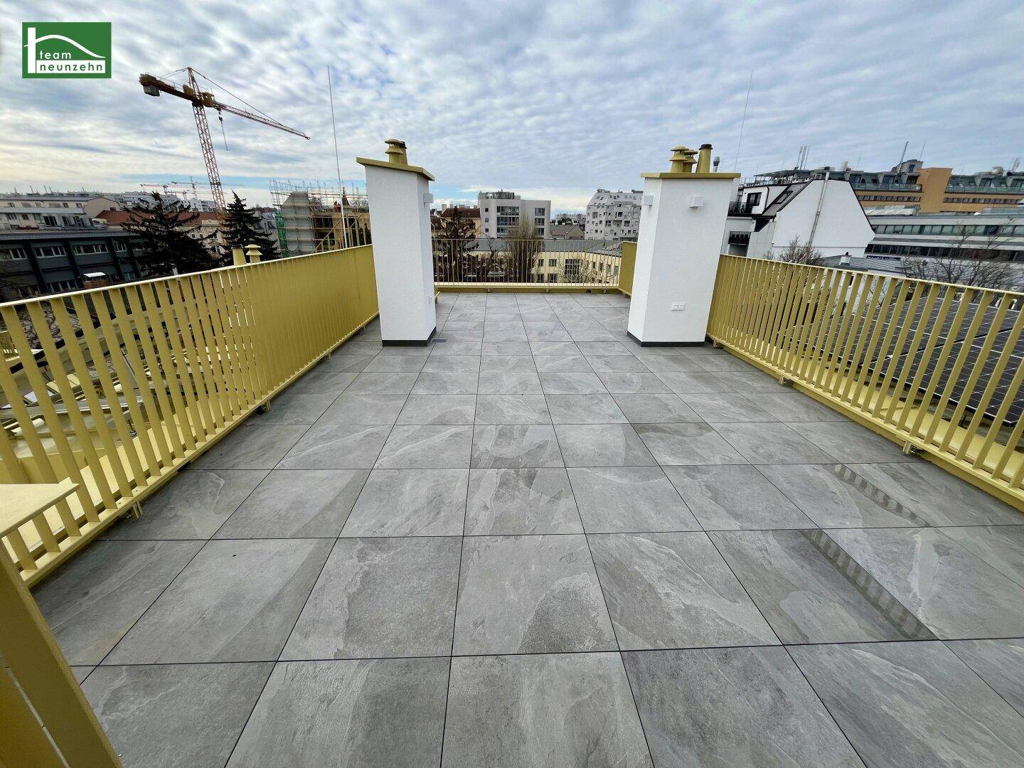 Geräumige Dachterrasse mit Fliesenboden und gelbem Geländer, bietet weite Stadtblicke.