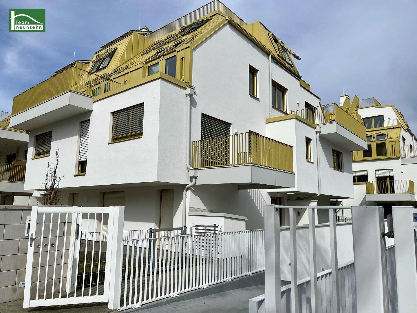 Moderne Wohnanlage mit weißer Fassade und gelben Akzenten, umgeben von einem Zaun.