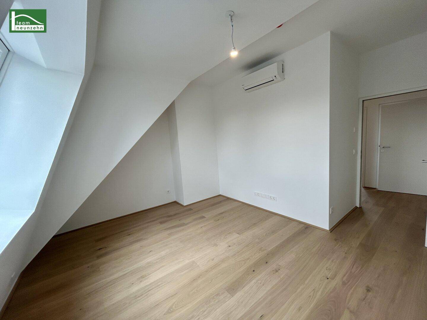 Geräumiges Zimmer mit Holzboden, Dachschräge und Klimaanlage, bereit zur Einrichtung.
