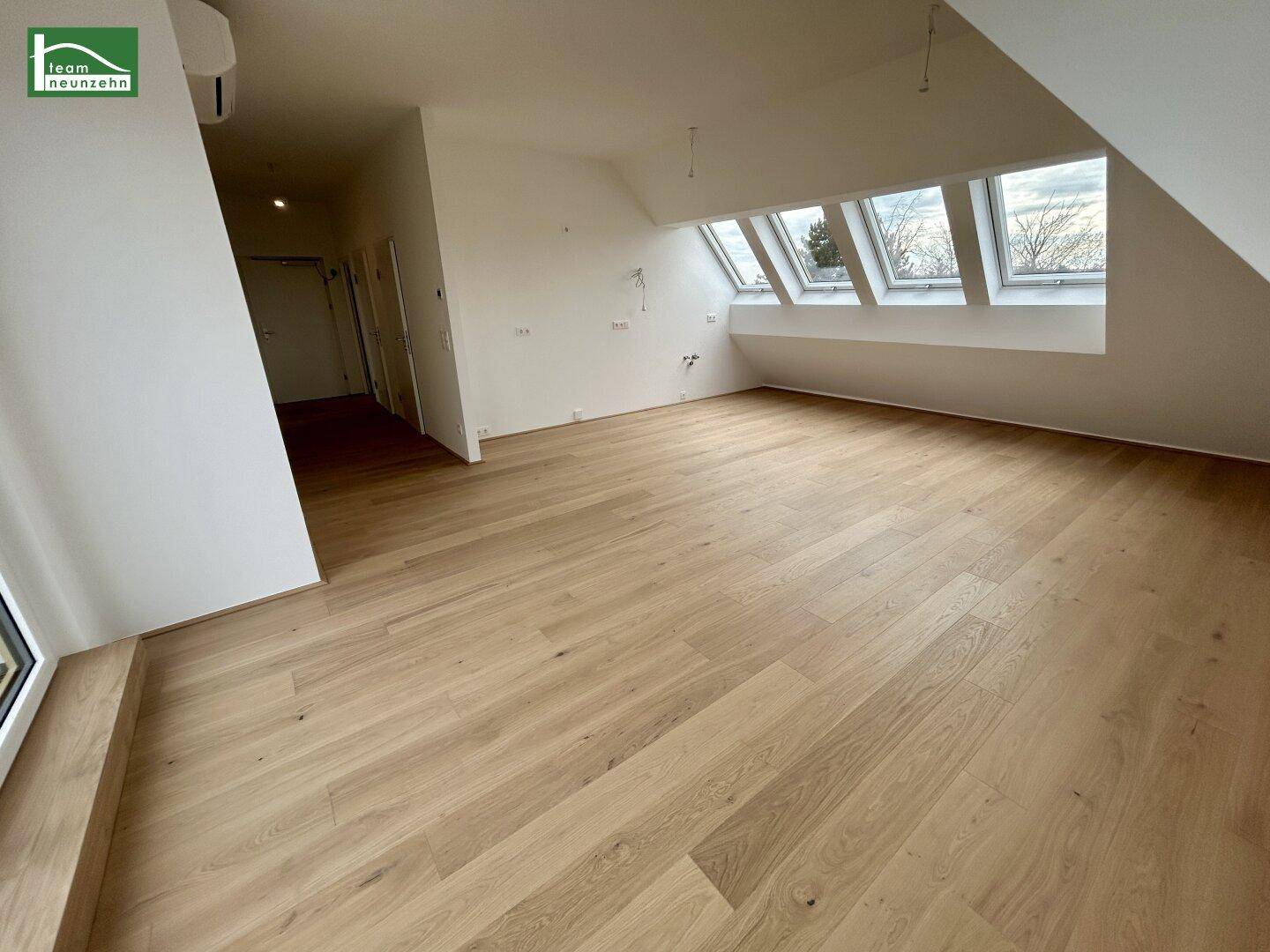 Geräumiger Wohnbereich mit Holzboden und mehreren Dachfenstern, lichtdurchflutet.