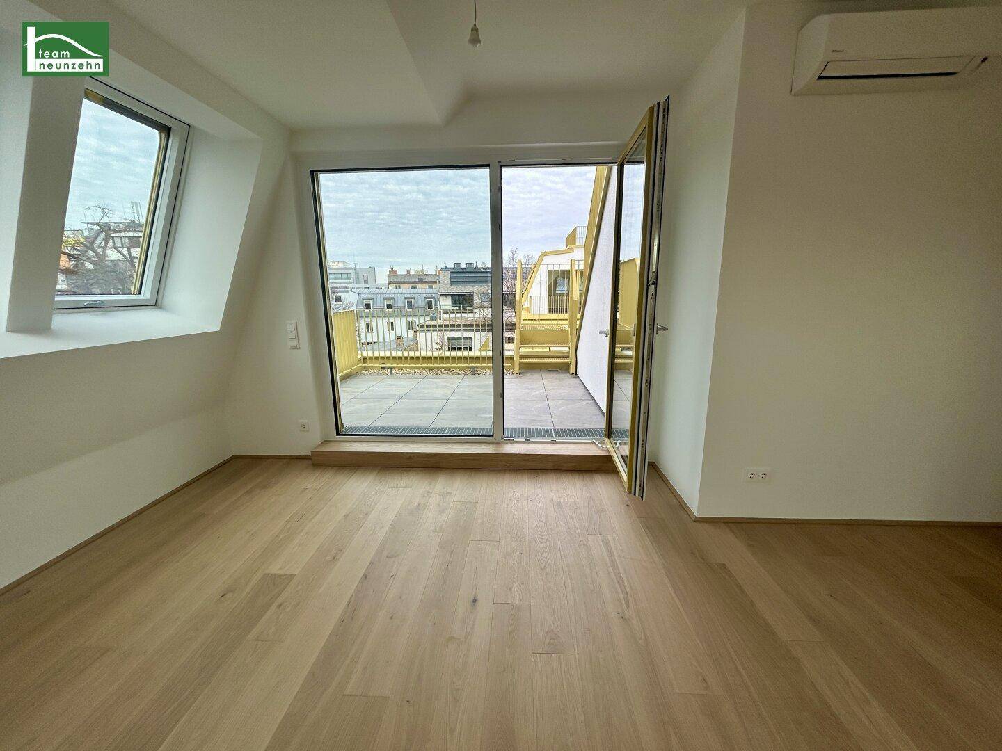 Heller Raum mit Holzboden und Zugang zu einer großen Dachterrasse mit Stadtblick.