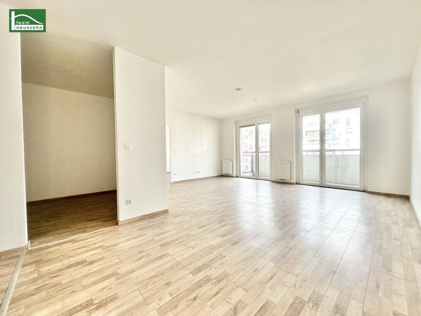Geräumiges, helles Wohnzimmer mit Laminatboden und doppelten Fenstertüren zum Balkon.