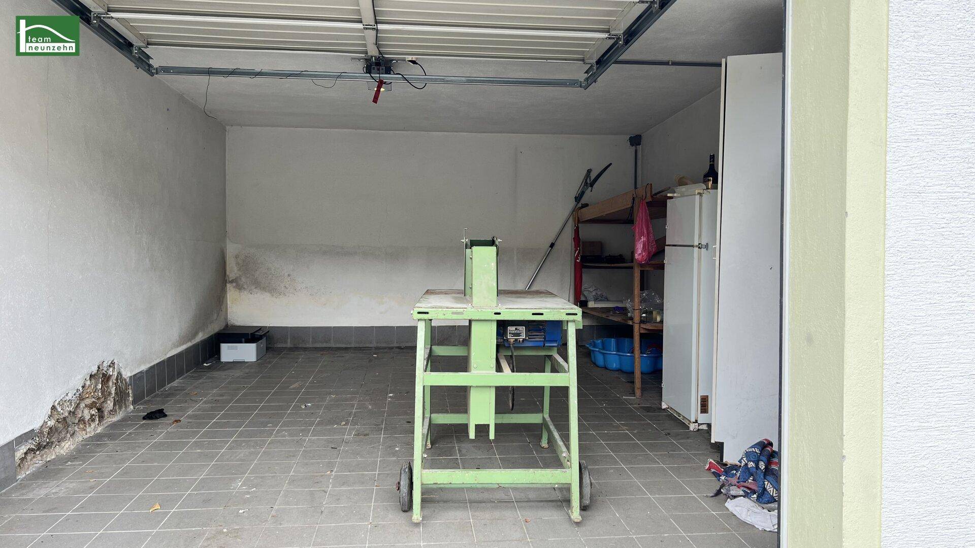 Leere Garage mit Fliesenboden und einem Rolltor, bereit zur Nutzung.