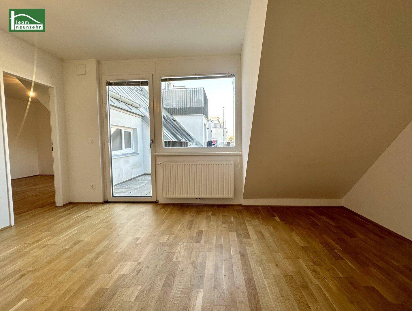 Leerer Raum mit Holzboden, Dachschräge und Zugang zu einem Außenbereich.