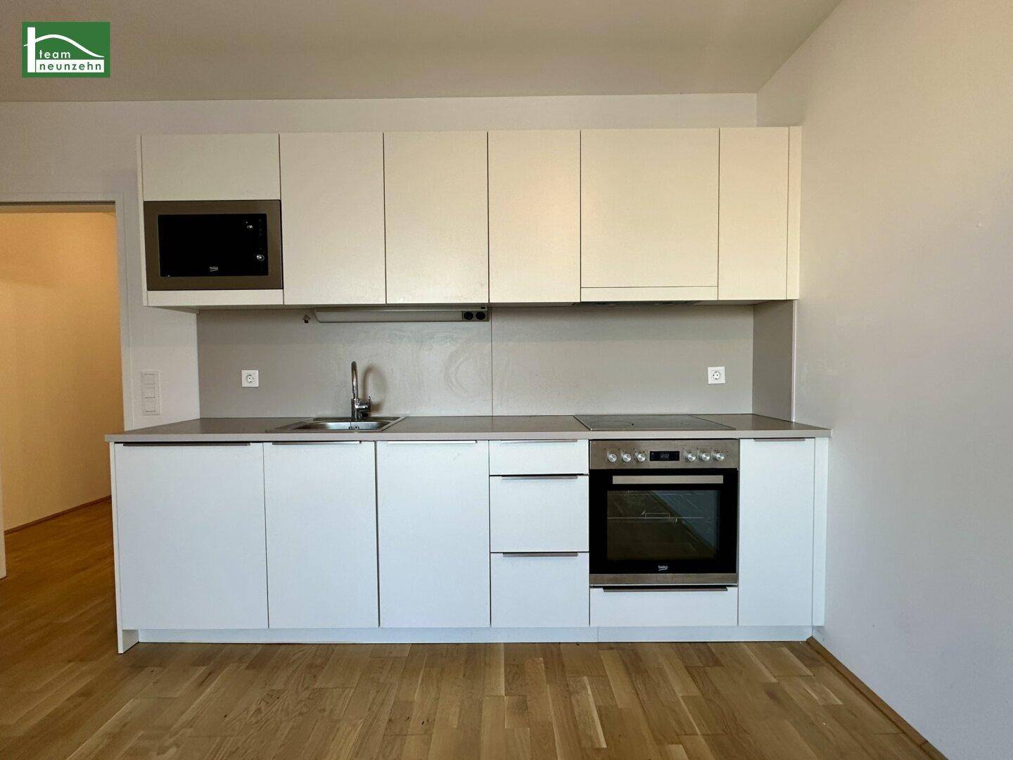 Moderne Küchenzeile mit weißen Schränken, integrierten Geräten und Holzboden.