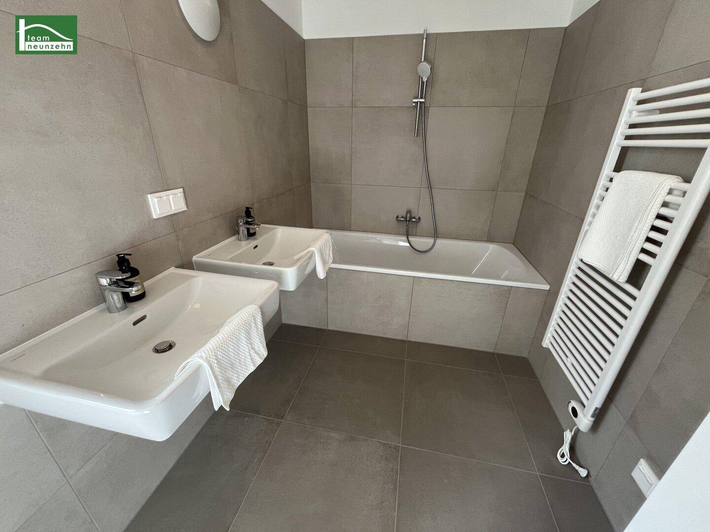 Modernes Badezimmer mit zwei Waschbecken, Badewanne mit Duschfunktion und beheiztem Handtuchhalter.
