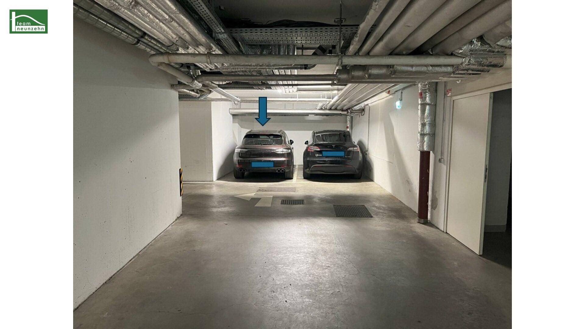 Tiefgaragenstellplätze mit zwei geparkten Autos und sichtbaren Versorgungsleitungen an der Decke.