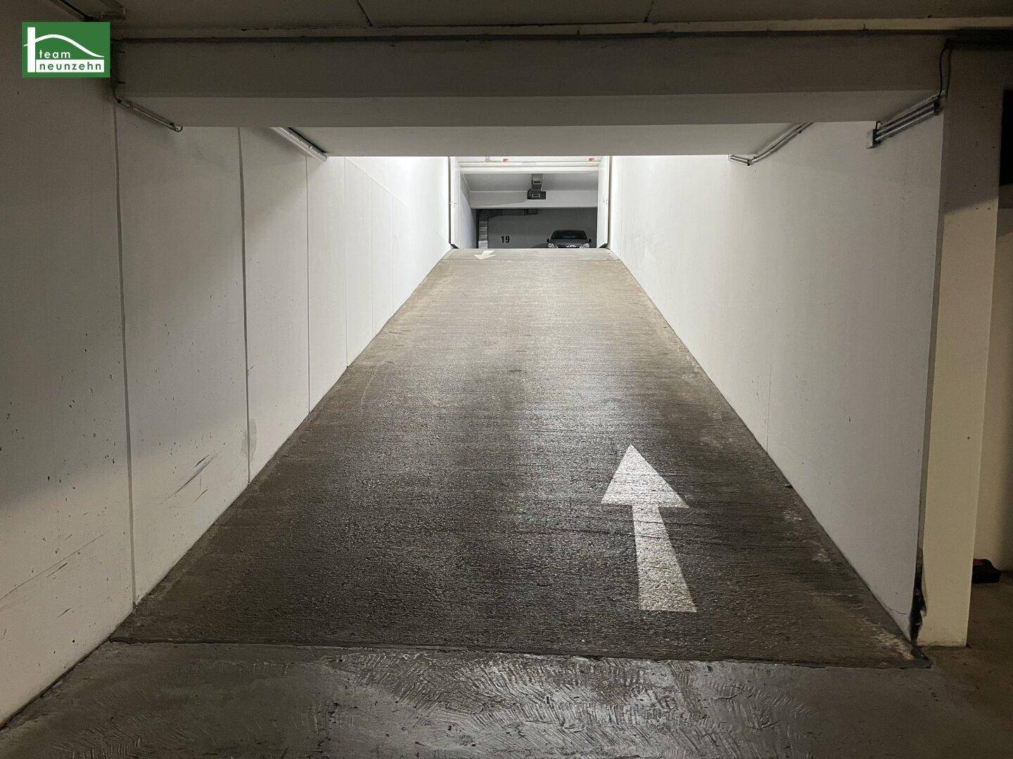 Einfahrtsrampe zu einer Tiefgarage mit Pfeilmarkierung auf dem Betonboden.