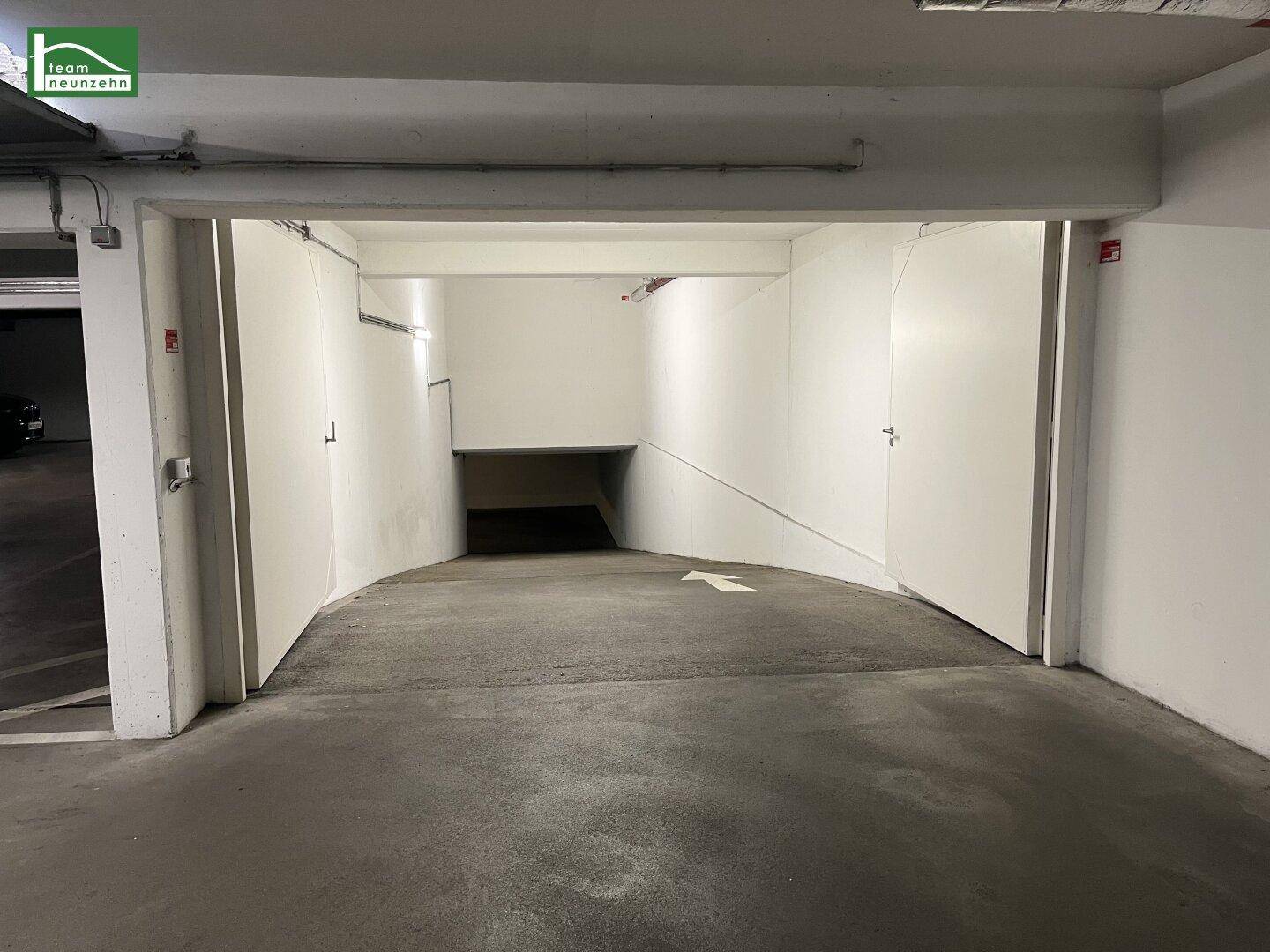 Gekrümmte Einfahrt in eine Tiefgarage mit weiß gestrichenen Wänden und Pfeilmarkierung.