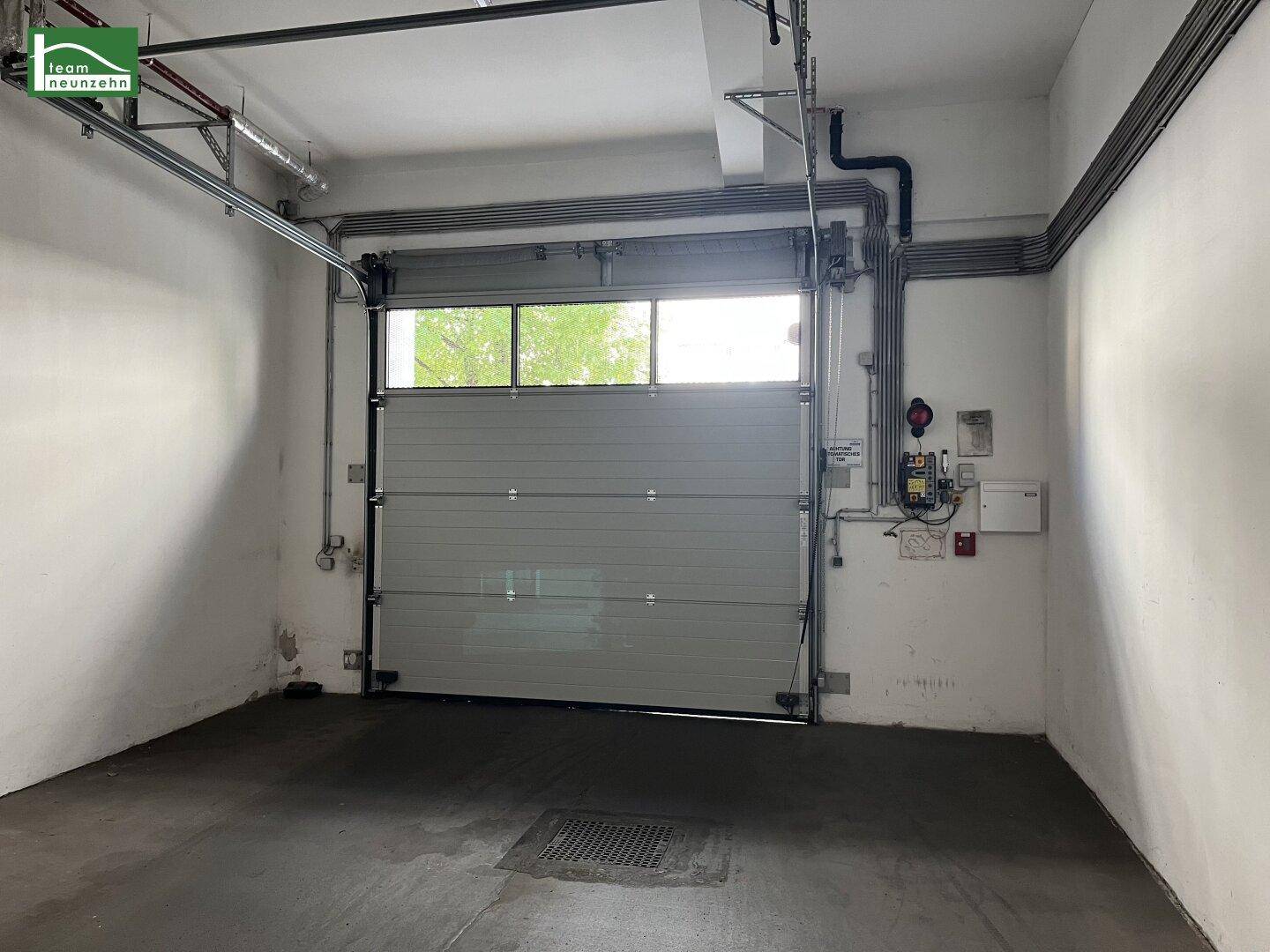Innenansicht einer Garage mit geschlossenem Rolltor und sichtbaren Installationen an den Wänden.