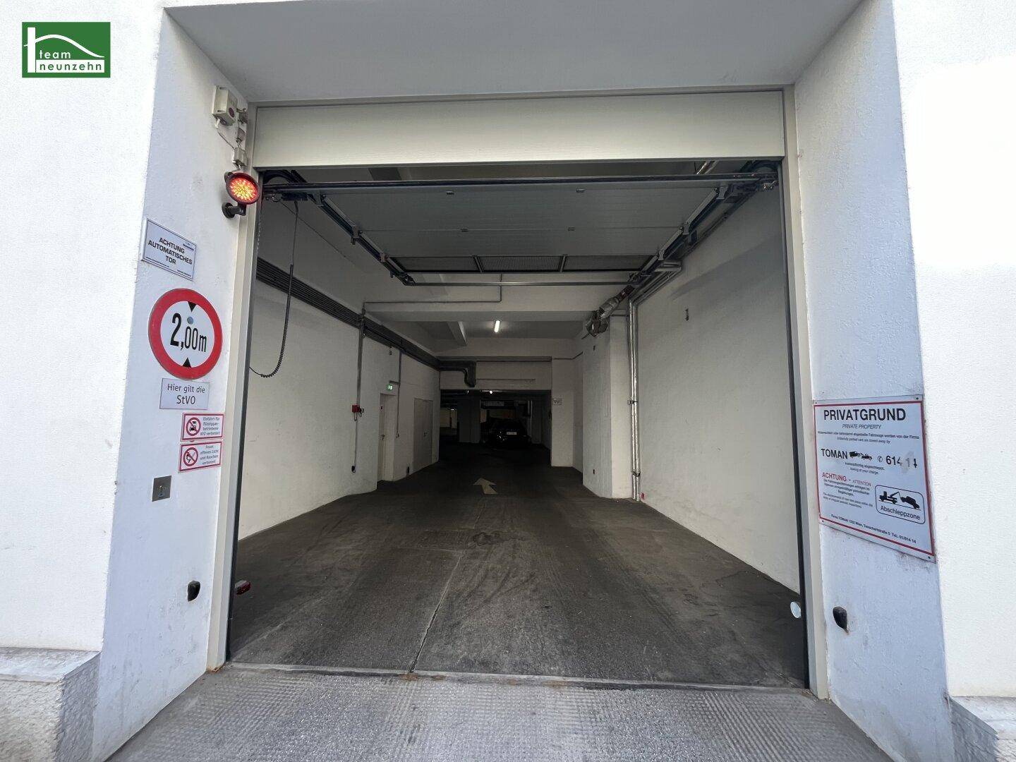 Einfahrt zu einer Tiefgarage mit Höhenbegrenzung und Hinweisschildern an der Gebäudefassade.
